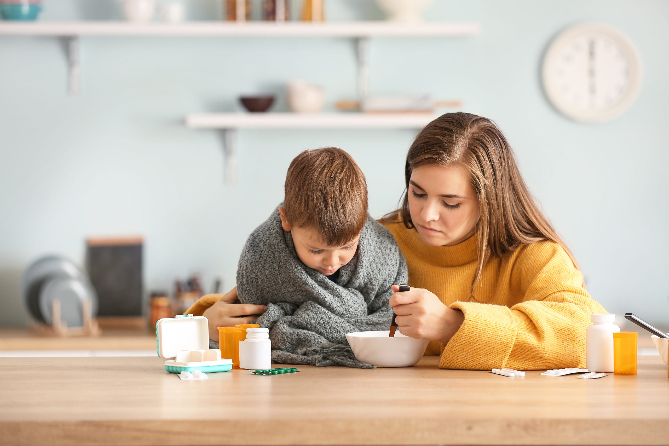 Mother feeding her sick son with chicken soup in kitchen