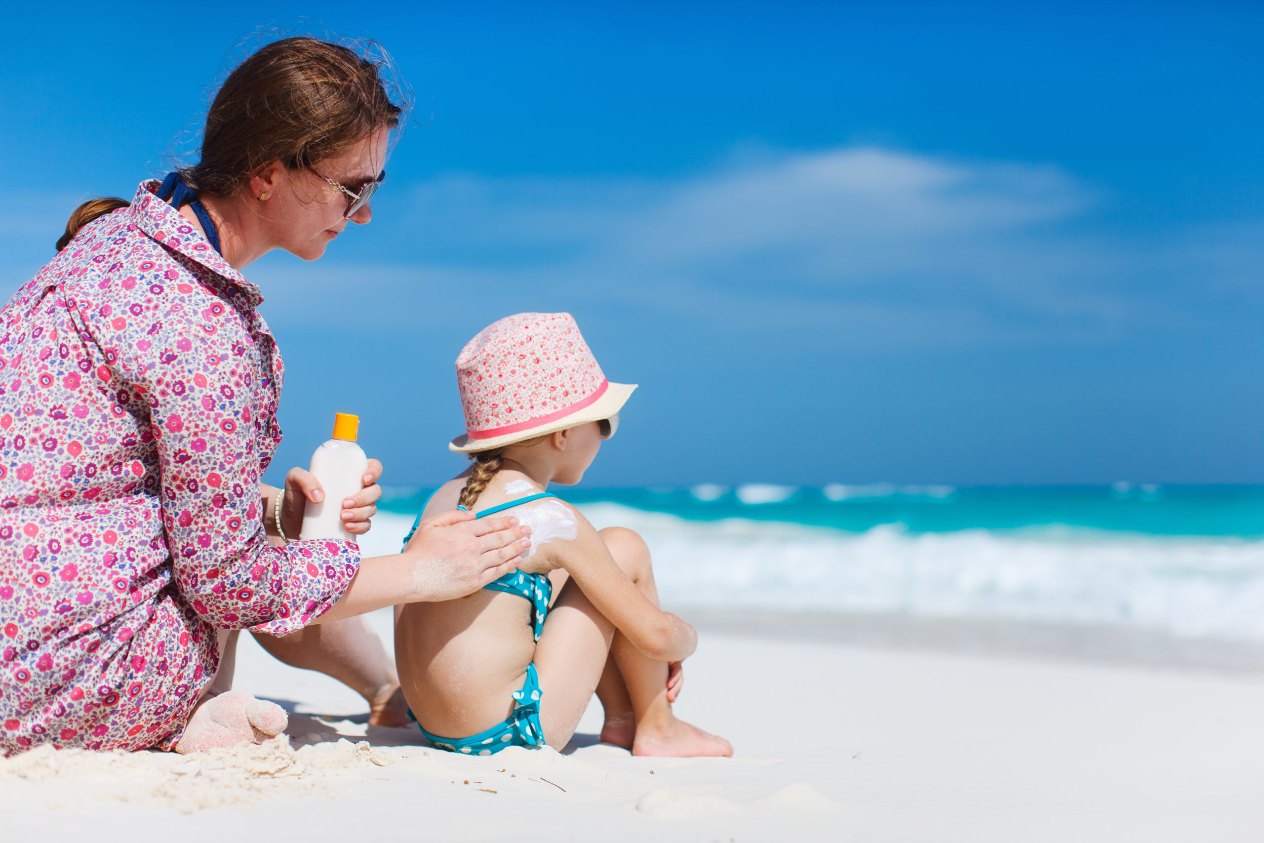 Mother applying sunblock cream on her daughters shoulder