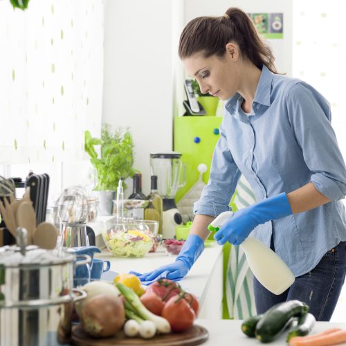 Woman cleaning and polishing the kitchen worktop with a spray detergent, housekeeping and hygiene concept