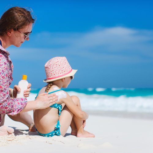 Mother applying sunblock cream on her daughters shoulder